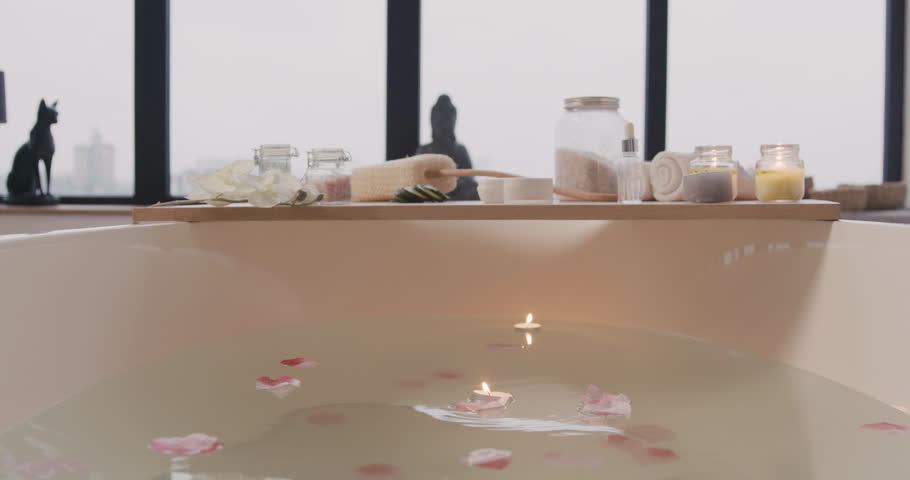 Camera focuses on a white bathtub with water, flowers And candles And wooden table with bathroom elements. | Shutterstock HD Video #1111913411
