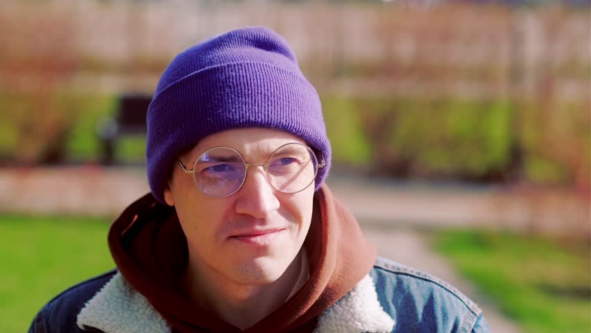 Young man wearing glasses drinking coffee in the spring park. Close-up shot.