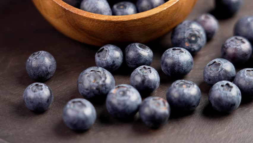 A pile of fresh blue bilberry on a brown board with wooden bowl. Ripe blueberries. Healthy bio food. Rotation Royalty-Free Stock Footage #1111915647