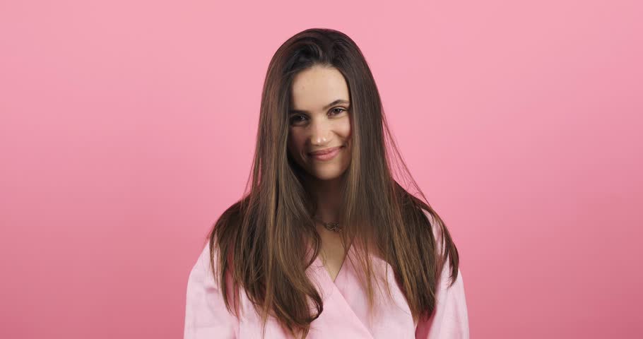 Cheerful happy joyful young woman, brunette loose hair cheerfully throws. Cute girl hands raised. Smiling face. Happy woman fix hair, look funny and funky isolated on pink background. | Shutterstock HD Video #1111918197