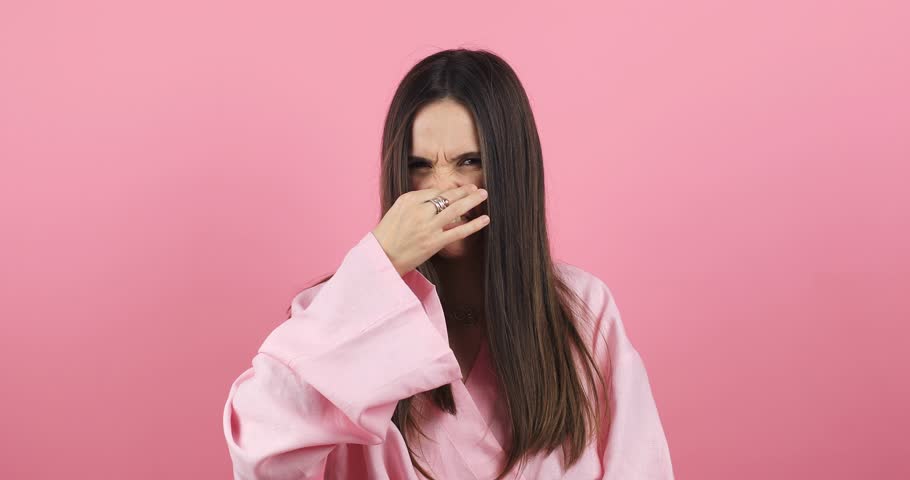Disgusting odor. Discontent brunette woman frowning face, smells something awful, feeling aversion, pink studio background. Girl face with aversion dislikes something unpleasant. Woman wear pink dress | Shutterstock HD Video #1111918541