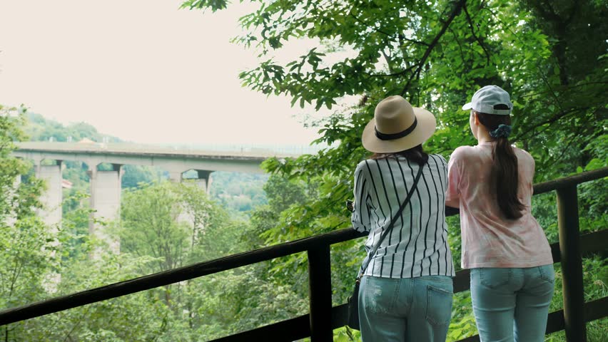 Mom and daughter. Two girls are looking at a beautiful landscape. A bridge for cars across the mountains. Summer in the park. | Shutterstock HD Video #1111919023
