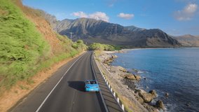 Summer vacation adventure tourism. Aerial view blue convertible car driving by coastal road along dramatic rocky shore towards volcanic mountains on Oahu island. Happy young couple traveling by Hawaii - Powered by Shutterstock - Get 15% off with code: PIKWIZARD15