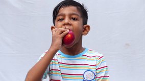 An Asian child is eating a red apple on an isolated white background. Fresh fruit-eating and enjoying concept 4k video.