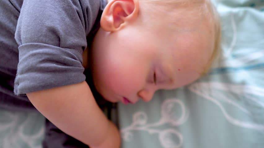 Peaceful adorable child sleeps alone on a bed in a room of the house. Baby is lying on a blue sheet, enjoying an afternoon nap. Concept of a sleeping baby. Health, pediatrics, carefree infancy concept | Shutterstock HD Video #1111920481
