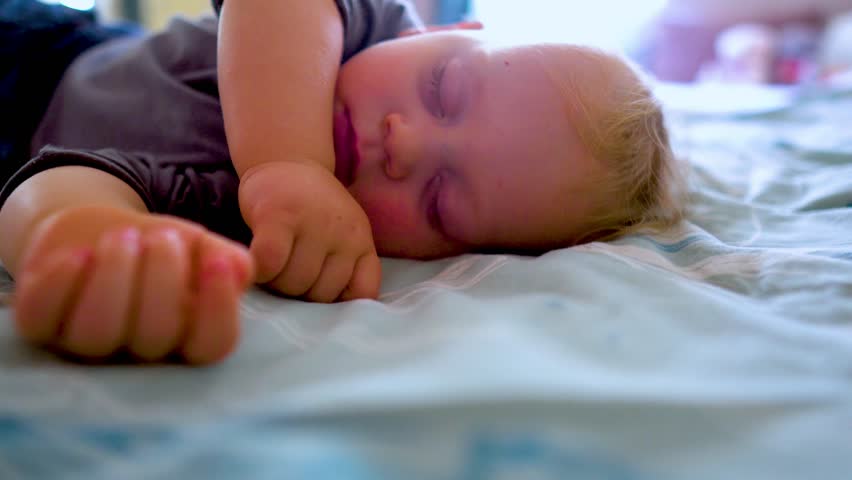 Peaceful adorable child sleeps alone on a bed in a room of the house. Baby is lying on a blue sheet, enjoying an afternoon nap. Concept of a sleeping baby. Health, pediatrics, carefree infancy concept | Shutterstock HD Video #1111920497