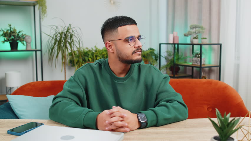 Portrait of happy calm Indian man at home table smiling friendly, glad expression looking away dreaming resting, relaxation feel satisfied good news, celebrate win. Arabian young guy in office room