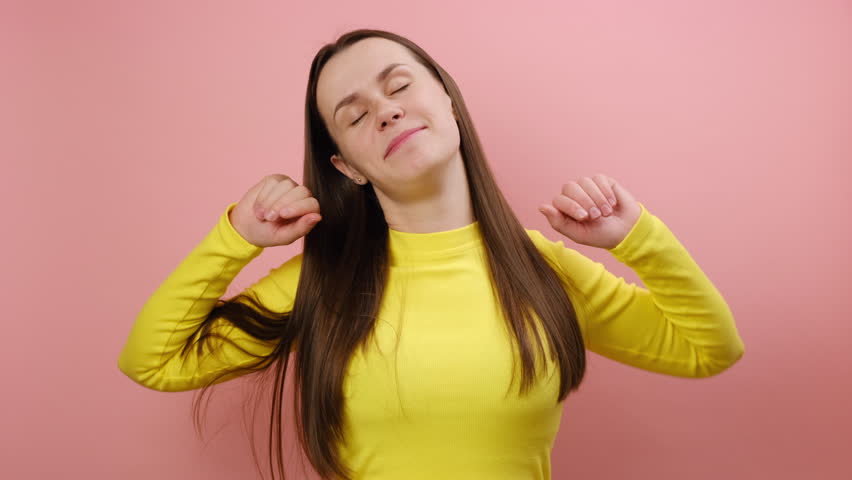 Portrait of sleepless young caucasian woman yawning and raising hands up, feeling fatigued, wakes up early in morning, wearing yellow sweater, posing isolated over pink color background wall in studio | Shutterstock HD Video #1111921495