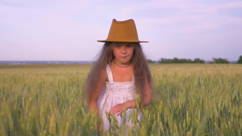 A little girl in a green field. A happy child enjoys the fresh air. A girl in a wheat field playing with young ears of wheat. | Shutterstock HD Video #1111922537