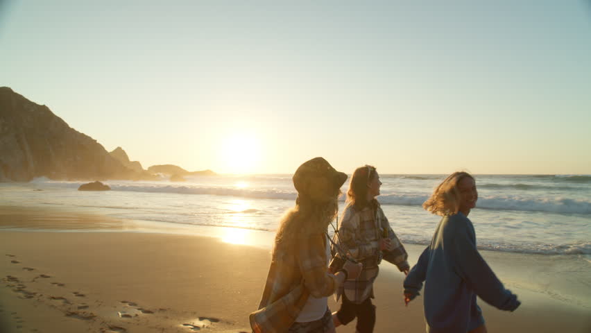 Three young women hang out at beach at sunset. Happy smiling friends run around barefoot in cinematic location near ocean. Photographer make photos of friends | Shutterstock HD Video #1111923869