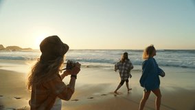 Three young women hang out at beach at sunset. Happy smiling friends run around barefoot in cinematic location near ocean. Photographer make photos of friends - Powered by Shutterstock - Get 15% off with code: PIKWIZARD15
