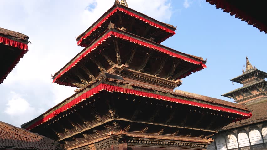 Old carved wooden roofs of palaces and temples on Durbar Square in Kathmandu, the capital of Nepal. Pigeon birds are flying in the square. World Heritage Site