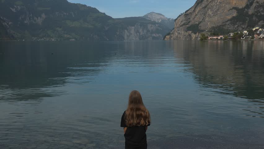 a young girl stay on stones on the shore of a lake in Switzerland and looks at the lake