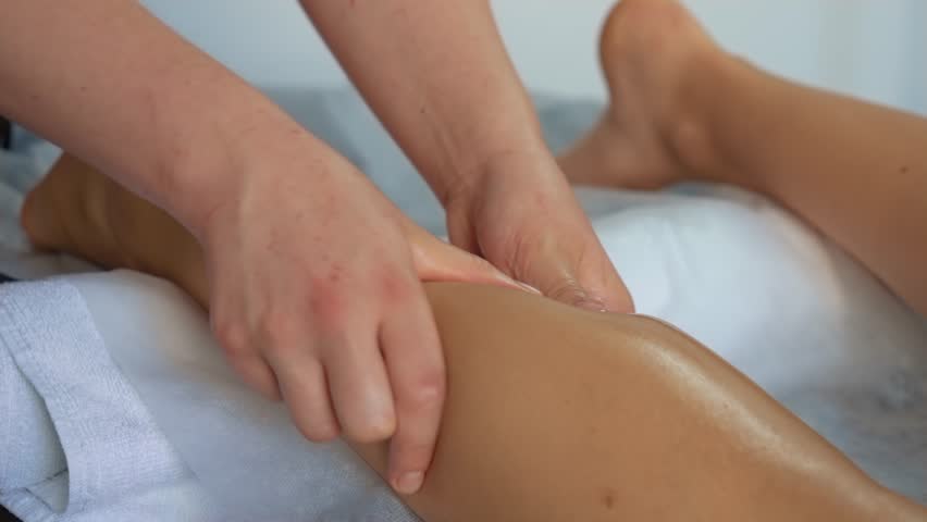 Masseuse massages, thigh and legs close up. Anti-cellulite massage in spa salon. Relaxing treatment. Masseur touching with warm hand body of female patient for body relaxation | Shutterstock HD Video #1111925183