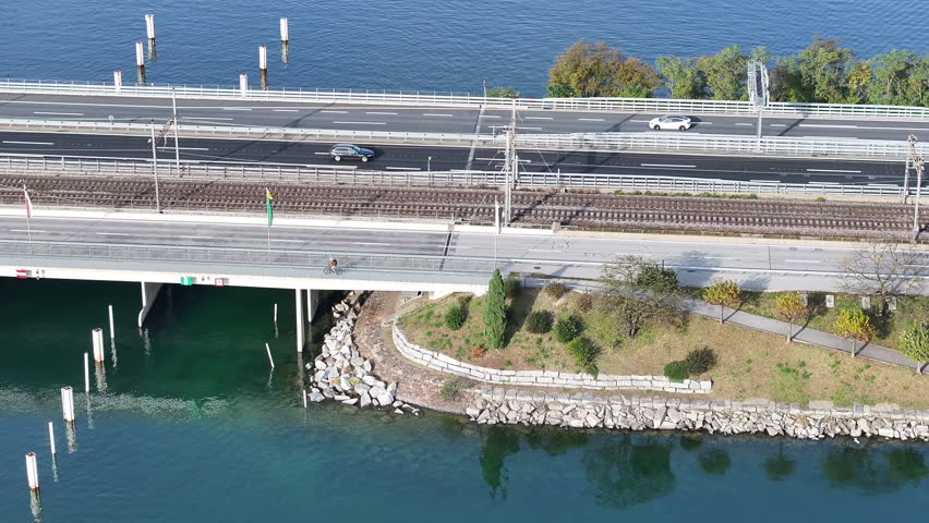 Aerial perspective of commuter riding e-bike along lakeshore next to road and railway. Tranquil fall scene crossing lake to work.