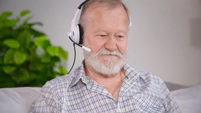charming elderly man with headset uses video calling on laptop to communicate with his old friends while sitting on sofa in cozy room - Powered by Shutterstock - Get 15% off with code: PIKWIZARD15