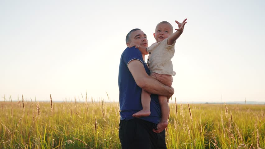Father with son in his arms in a clearing in nature. happy family childhood dream concept. parent holding son in arms in a meadow with tall grass. dad lifestyle and baby in the foreground sunset | Shutterstock HD Video #1111926663