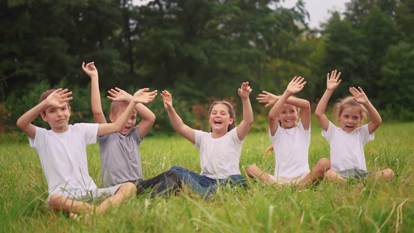 Children sit on the grass in the park with their hands up. happy family childhood dream concept. kids are resting in a park in the meadow sitting on the lifestyle grass and stretching their hands up | Shutterstock HD Video #1111926667