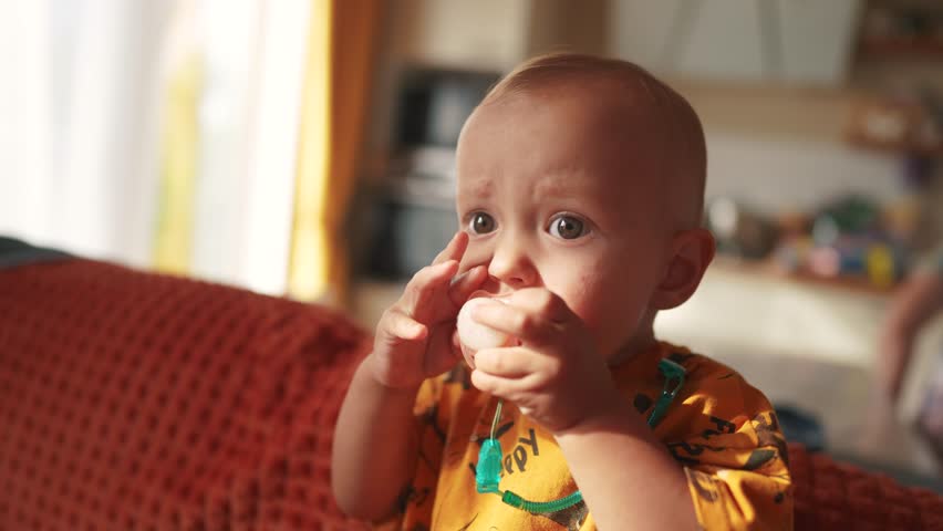 A small newborn sits on the couch with a pacifier in his mouth. happy family childhood dream concept. a little child with a pink pacifier sits and looks at the lifestyle camera baby face close-up | Shutterstock HD Video #1111926677