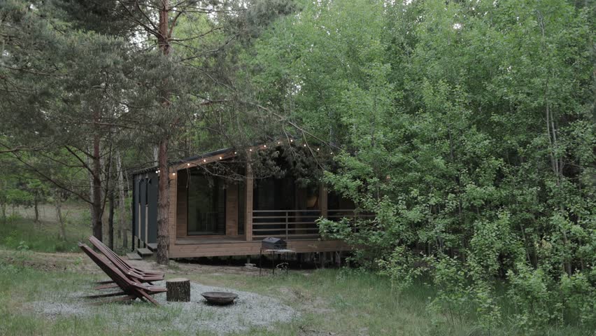 Wood building hidden in the forest, green grass, cozy campfire place in front of the house. Wooden scandinavian house, slow motion.