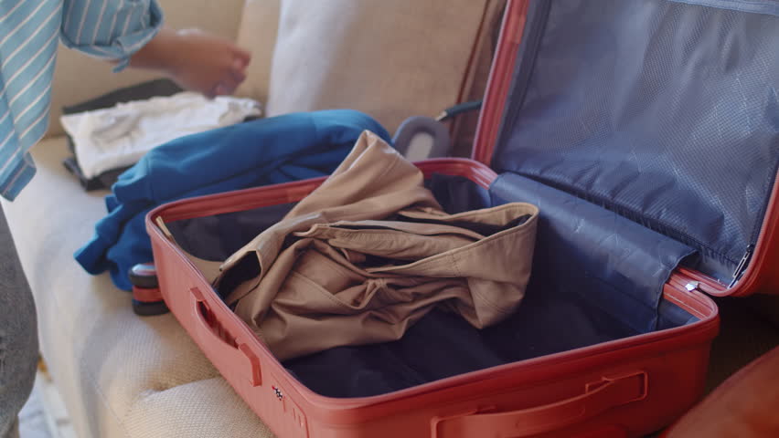Young woman folds prepared clothes, laptop and headphones into a suitcase laying on a couch and closes it during preparation to the vacation close up | Shutterstock HD Video #1111928215