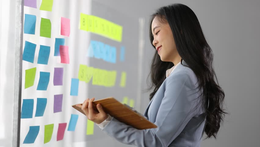 Creative young Asian woman thinking and planning a startup business with paper stickers on a transparent board. | Shutterstock HD Video #1111929911