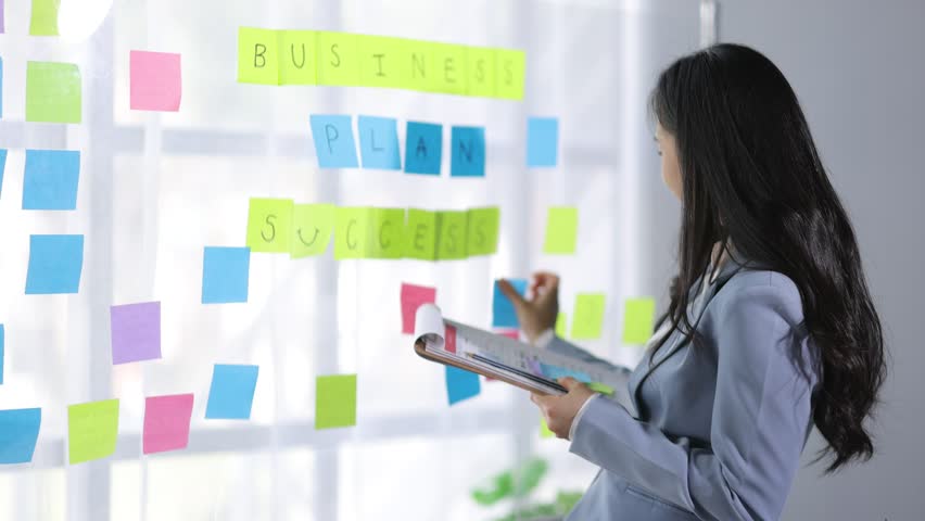 Creative young Asian woman thinking and planning a startup business with paper stickers on a transparent board. | Shutterstock HD Video #1111929965