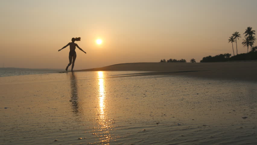 Young woman in swimsuit running on sand beach near ocean at sunset. Beautiful young girl jogging on sea shore with waves and enjoying vacation. Concept of relaxing on summer holiday. Slow motion | Shutterstock HD Video #1111930287