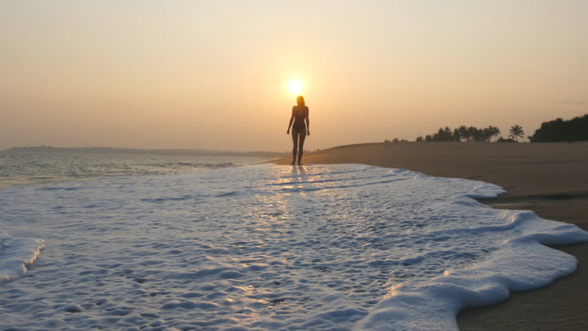 Young woman in swimsuit running on sand beach near ocean at sunset. Beautiful young girl jogging on sea shore with waves and enjoying vacation. Concept of relaxing on summer holiday. Slow motion | Shutterstock HD Video #1111930289