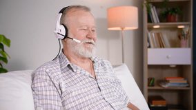 an elderly man with a headset talking on a video call on a laptop with his family while sitting in a cozy room