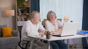 online communication, joyful elderly parents use laptops video calling to communicate with their family via video call while sitting at the table in the room