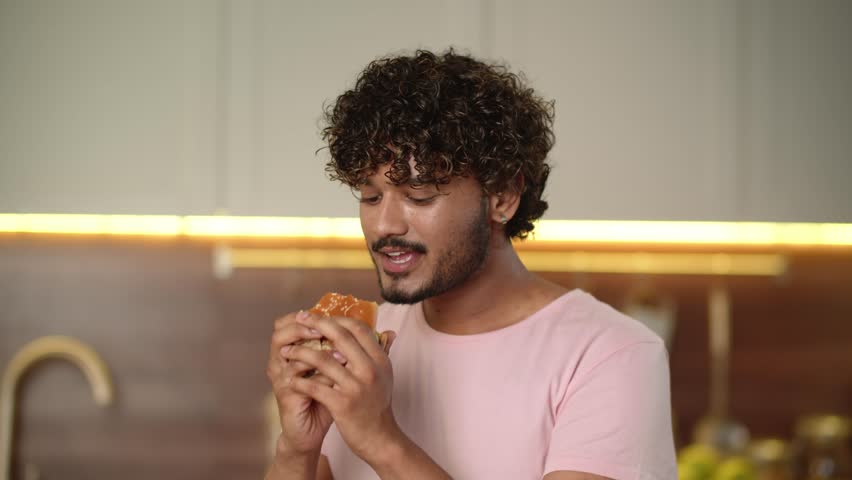 Concept of fast food delivery. Cheerful guy holding big burger and showing okey symbol approve his cool taste. Young man eating big hamburger gesturing ok feedback. Cheat meal at home Royalty-Free Stock Footage #1111930375