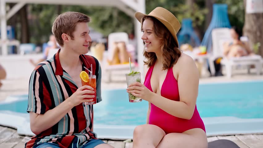 Satisfied people on pool party drinking fresh cocktail in poolside. Young boyfriend and girlfriend sitting sunbeds sunbathing drinks mohito, aperol near water. Alcohol pub with open swimming pool | Shutterstock HD Video #1111930393