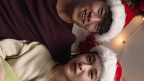 Vertical Screen: couple in santa hat making video call and talking to camera greeting family on Christmas and New Year holidays. female and male lovers sitting on couch with glasses of wine - Powered by Shutterstock - Get 15% off with code: PIKWIZARD15