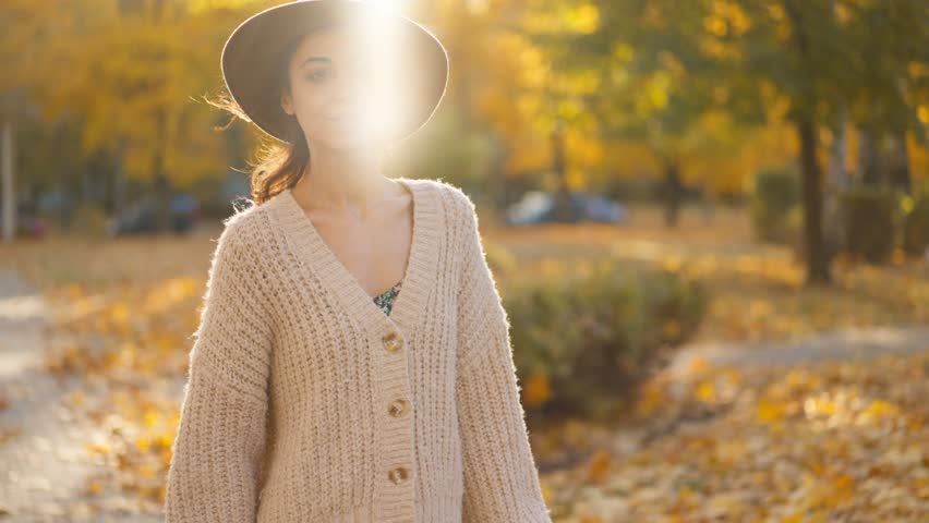 Stunning young brunette woman in autumn park with yellow foliage against sunset sun with sunflare. stylish attractive girl walks in park at warm fall day. slow motion 4k footage | Shutterstock HD Video #1111932769