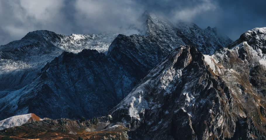 Beautiful aerial slow speed zoomed 4k mountain view of Austrian Alps. High quality prores footage in daylight, rocky steep hill with contrasting snow and stormy sky