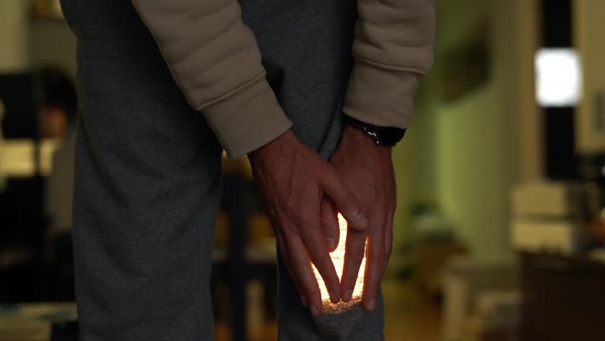 A man in pants holding his sore knee. The pain flashes with a bright light. | Shutterstock HD Video #1111935001