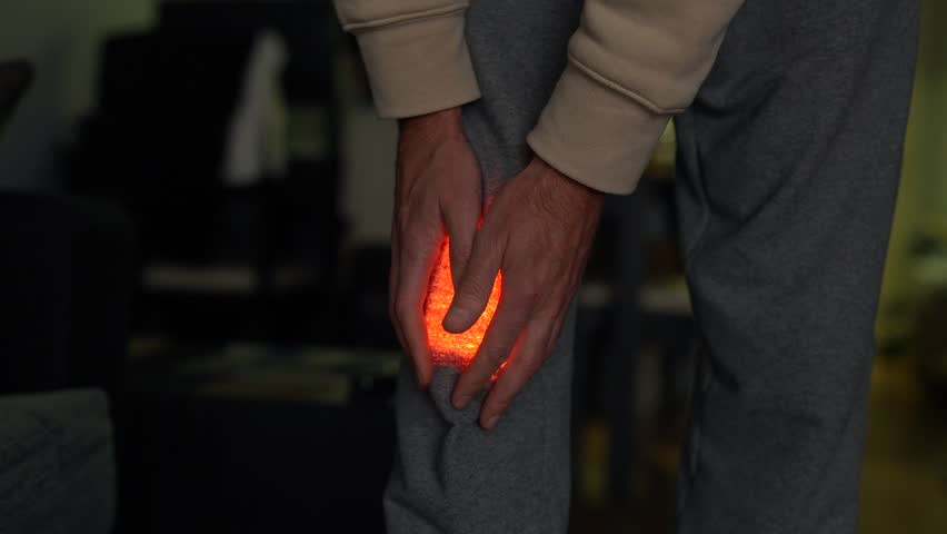 A man suffers from knee pain close-up. The inflamed area glows red. | Shutterstock HD Video #1111935003