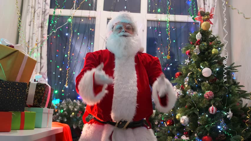 Cheerful Santa Claus is working in his workshop, putting magical gifts flying into his hands into a large pile to congratulate everyone on Christmas holiday and decorate the party with festive mood.