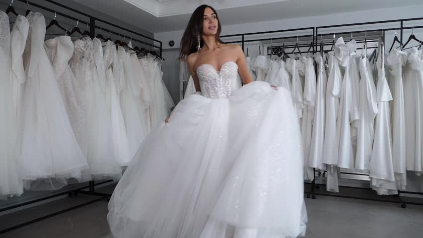 A beautiful bride in a long elegant white dress, the fabric of which flutters in the air in the wedding salon. A playful woman poses in front of the camera, spinning in a fabulous dress. Slow motion.