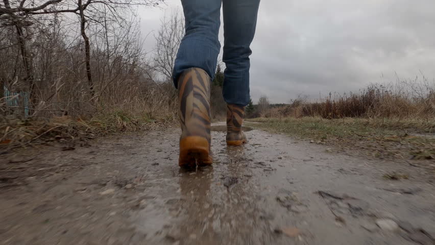 Man in rubber boots walking along dirt road with puddles, rear view. | Shutterstock HD Video #1111939377