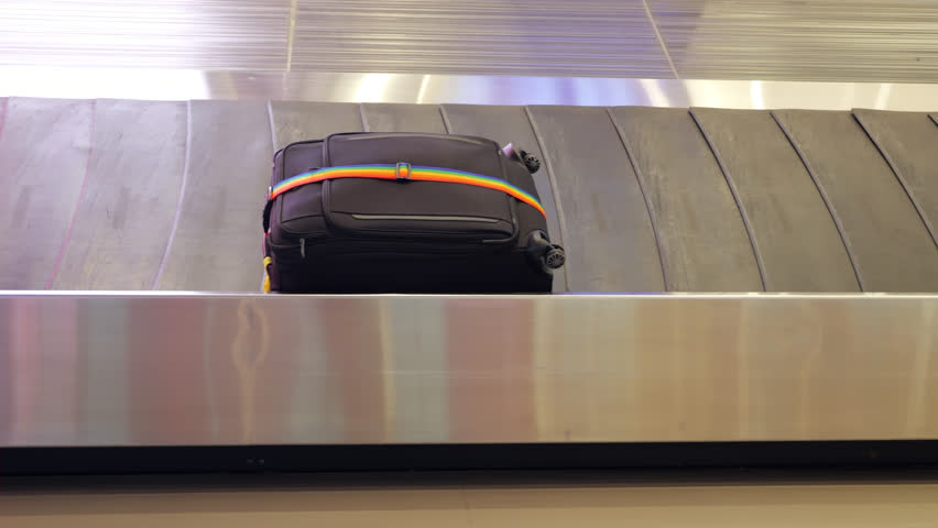 Black textile suitcase glides on moving baggage carousel, wrapped with distinctive rainbow ribbon for security. The conveyance is captured in parallel motion, simple yet large and regular luggage | Shutterstock HD Video #1111940947