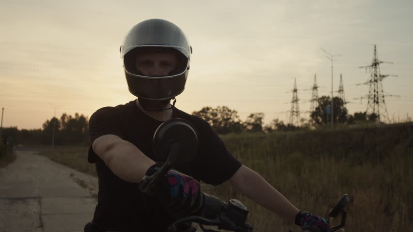 The motorcycle driver stands in the middle of the road strictly looking forward in the sun