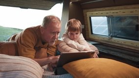Grandfather and grandson enjoy reading on a tablet while camping near a field dotted with solar panels - Powered by Shutterstock - Get 15% off with code: PIKWIZARD15