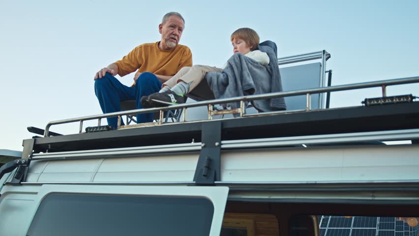 Grandson and grandpa chat at solar powerplant, on the camper rooftop at dusk | Shutterstock HD Video #1111949717