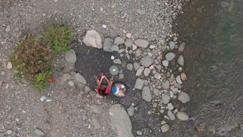 Filipino Woman Washing Dishes in Shallow River. Aerial, straight down. Philippines. 