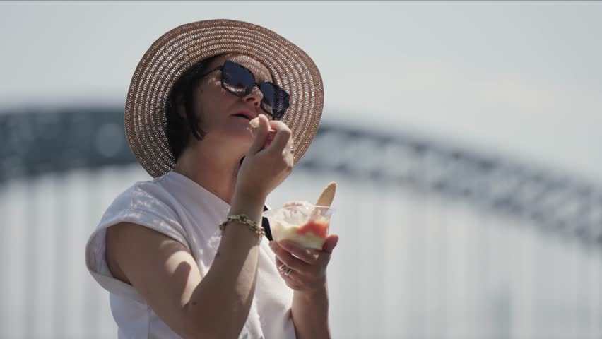 Happy young beautiful woman wearing hat and glasses eating a big spagetti ice cream on the street, selective focus cinematic shot Royalty-Free Stock Footage #1111951903