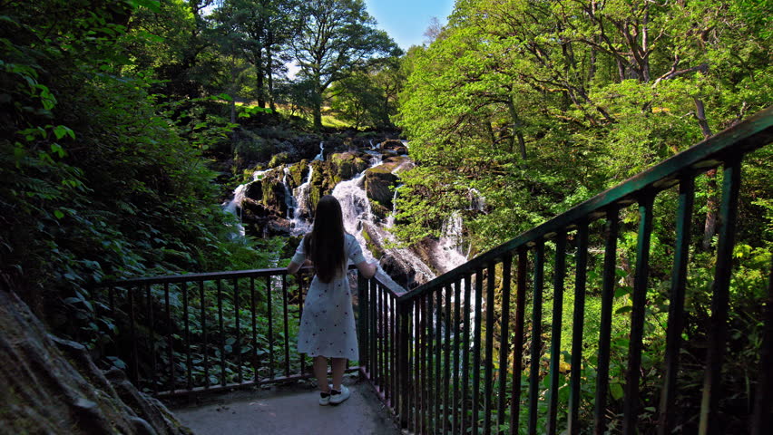 Beautiful woman visits Rhaeadr Ewynnol Swallow Falls Waterfall, Tourist attraction in Wales. Female tourist looking at the churning waterfalls in a picturesque, wooded setting in Wales. Royalty-Free Stock Footage #1111952627