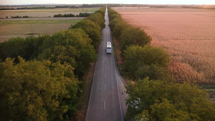 Aerial drone high angle footage of traffic driving along a rural farmland road surrounded by trees on a summer afternoon. Sunset flyover shot of cars and trucks moving along a picturesque road.
 Royalty-Free Stock Footage #1111952899