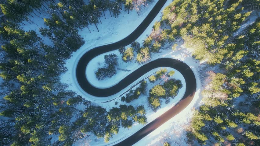 Twisted road in winter forest. Asphalt road serpentine and snowy landcape around. Aerial 4K footage from drone flight